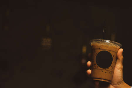 Hand holding iced mocha with straw in plastic cup at cafe restaurantの写真素材