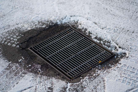 Sewer manhole on a city sidewalk covered with snow