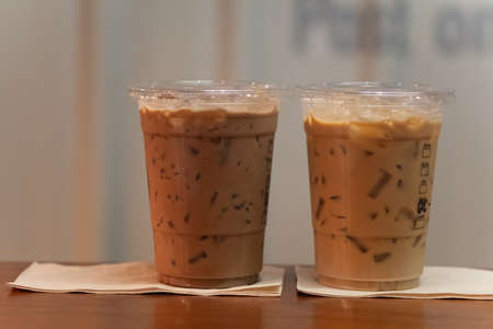 Close up of two take away plastic cup of iced mocha coffee and iced espresso on wooden table