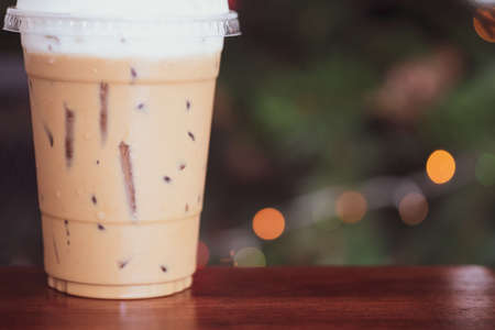 Iced latte coffee with milk froth in transparent plastic cup on wood tableの写真素材