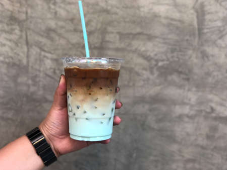 Hand woman holding a glass of iced coffee with mint syrup with cement wall backgroundの写真素材