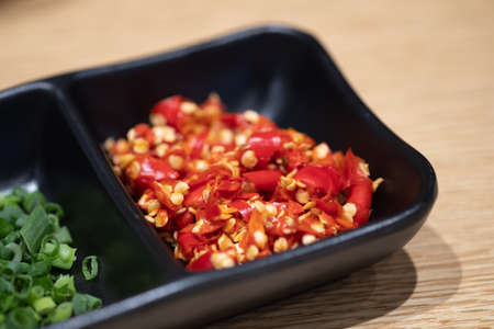 Seasoning of shabu, slice chili, green onion in a black bowl on wood table