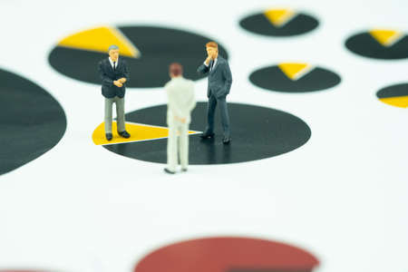 Miniature group of businessman meeting and standing on pie chart as business yearly review of...