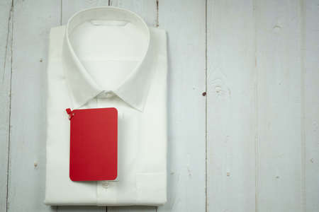 Classic folded white men's shirt with empty red tag on wood backgroundの写真素材