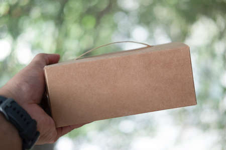 Hand holding a brown cardboard box. Delivery mail man giving parcel box to recipientの写真素材