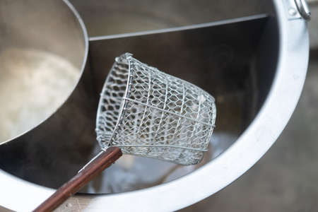Traditional Thai steel wire mesh noodle strainer on a hot noodle pot. Close up