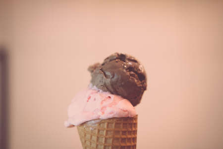 Wafer cone with two scoops of ice cream strawberry and chocolate in young hand