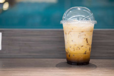 Ice milk tea in plastic glass on wooden table at cafe shop