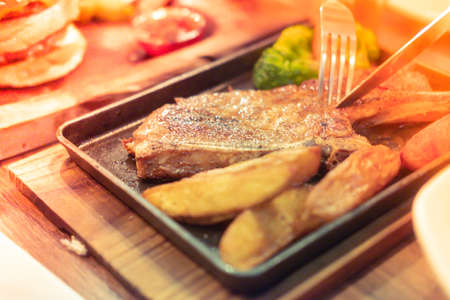 Hands are holding a fork and knife to cut pork chop steakの写真素材