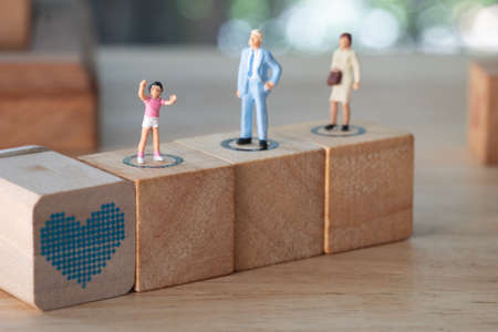 Miniature family on wood block. Son stand in front of his protect parents