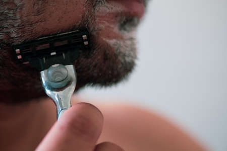 Man is shaving beard his face in bathroom in morning. Close upの写真素材