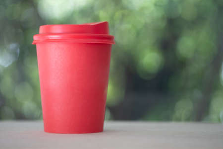 Red take away paper cup with red cover for hot drink on blur nature background