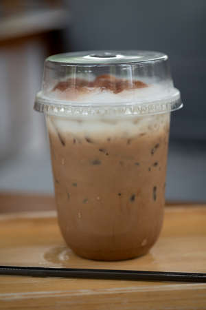 Iced coffee mocha in clear plastic glass served on wood tray
