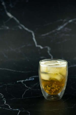 Glass of beer with ice on black marble background