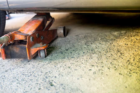 The orange hydraulic jack is lifting the car in the auto repair shop.の写真素材