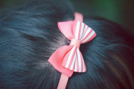Cute pink bow with striped pattern on a head of cute girlの写真素材