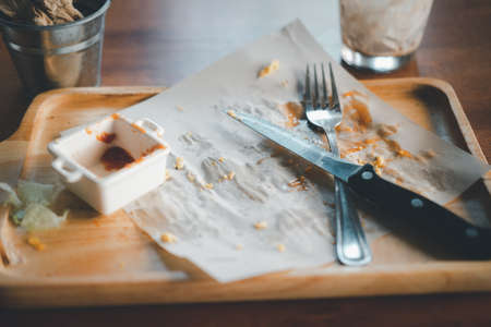 Leftover food on a wooden plate with a knife and fork. Close upの写真素材