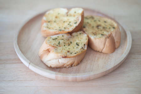 Wooden plate with delicious homemade garlic bread on wooden table