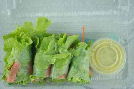 Salad roll vegetables wrapped in flour on clear plastic box with salad dressing