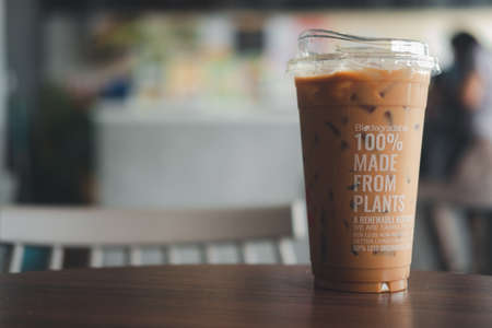 Bangkok, Thailand - April 25, 2020: Closeup of iced coffee cup in 100% made from plants put on wooden table in coffee shop. A beverage container that can be decomposed naturally in Inthanin coffee shops.のeditorial素材