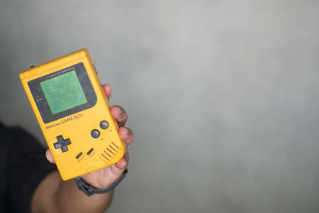 Samut Prakan, Thailand - April 26 2020 : Young man hand holding of an original Nintendo handheld video game device Game boy (1989).のeditorial素材