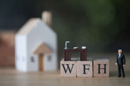 Miniature businessman standing with wood block WFH and home. Concept of work from home