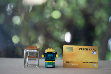 Miniature student table and school bus with credit card on wood table. Concept of pay fees for...