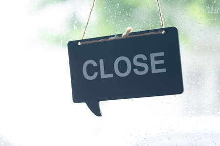 A sign hanging off Coffee shop door with raindrop on window