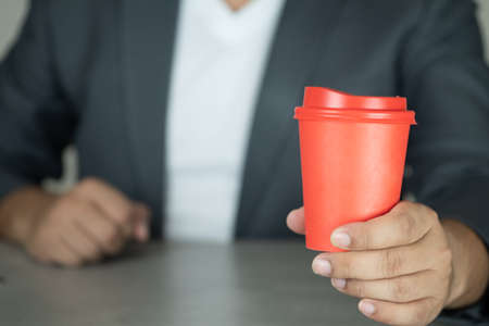 Handsome businessman in suit show red paper cup hot coffee or teaの写真素材