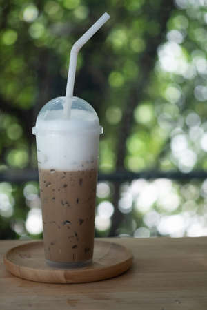 Iced coffee in a tall glass with milk on wood table