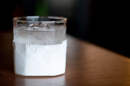 Glass of cold water wrapped in tissue paper on wood tableの写真素材