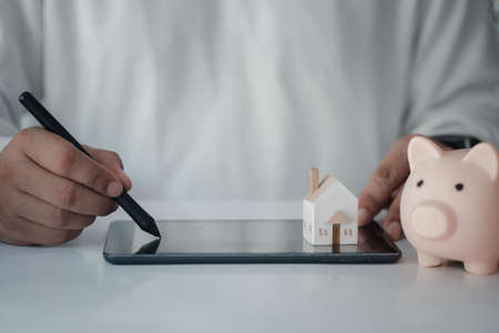 Businessman using tablet with piggy bank and home for planning saving money. Finance and money saving for the future conceptsの写真素材