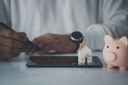 Man digital using pen for planning in the future on tablet with miniature home and piggy bank. Concept of planning in lifeの写真素材