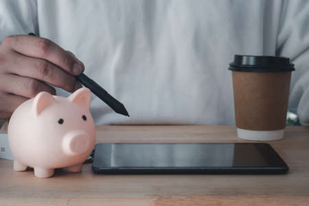 Young man use digital pen on tablet with pink piggy bank on wood tableの写真素材