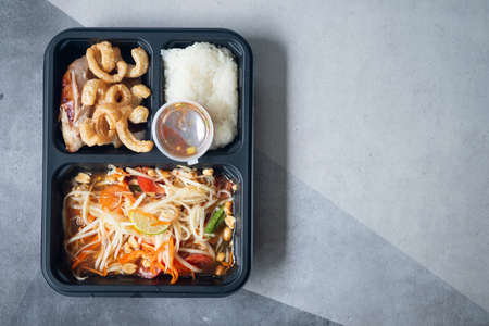 Set of papaya salad with sticky rice, grilled chicken and pork rind in take away lunch boxの写真素材