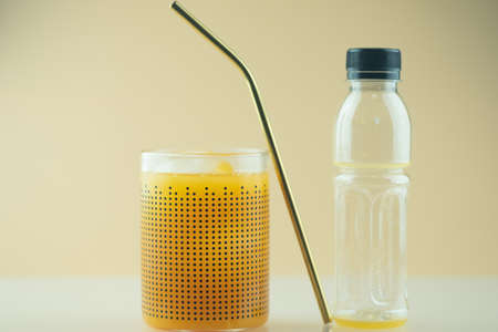 Fresh orange juice in glass pour from plastic bottle with gold straw