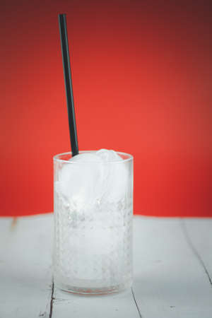 Empty glass with ice cubes and black straw in glass on red backgroundの写真素材
