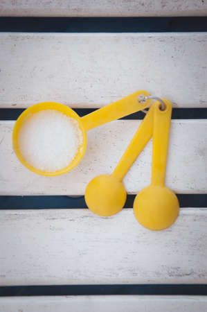 Yellow measuring spoons with sugar on white wood tableの写真素材