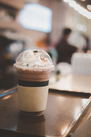 Closeup of takeaway plastic cup of iced cocoa with whipped cream on top.