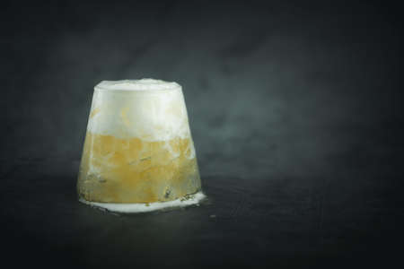 Cold foamy beer in a small glass and a black background with blank space for text
