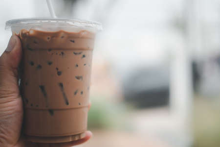 Hand holding iced mocha with straw in plastic cup at garden blur cafe restaurant in hot sunny dayの写真素材