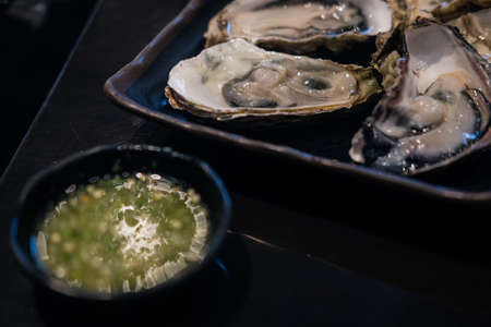 Close up a black tray of raw fresh oysters served with seafood sauce