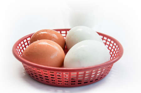 Fresh of brown eggs and white eggs (salted eggs) in red basket on a white backgroundの写真素材