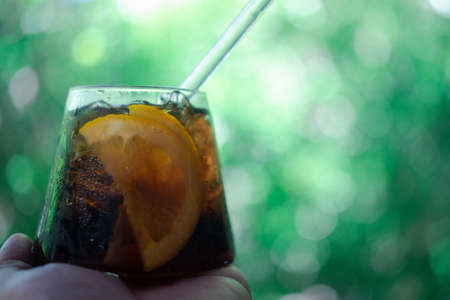 Cool soft drink with orange slices inside glass on hand arrange on blur nature background