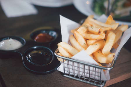 Basket of french fries served with sauce on table in restaurantの写真素材