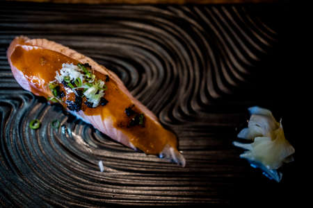 Grilled salmon sushi a bit topping with sauce and black caviar served on black plateの写真素材