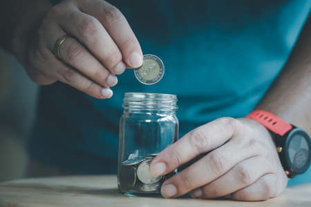 Man hand putting Thai coins in glass jar, idea saving money conceptの写真素材