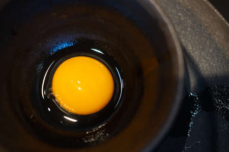Close-up raw uncooked egg in black bowl. Ingredient for cooking
