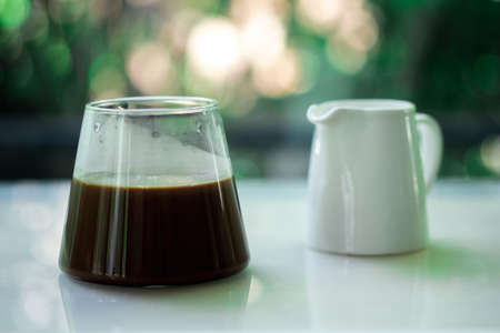 Hot black coffee in glass with mini milk jar on tableの写真素材