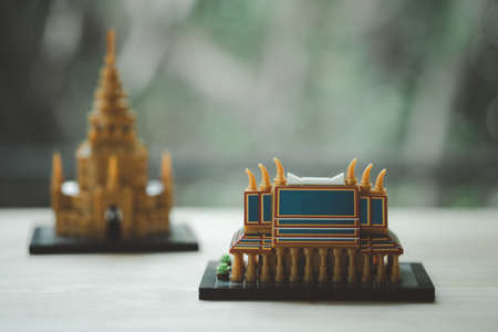 Miniature plastic block of Thai chapel on wood table and golden pagoda background. Concept of travel Thailandの写真素材